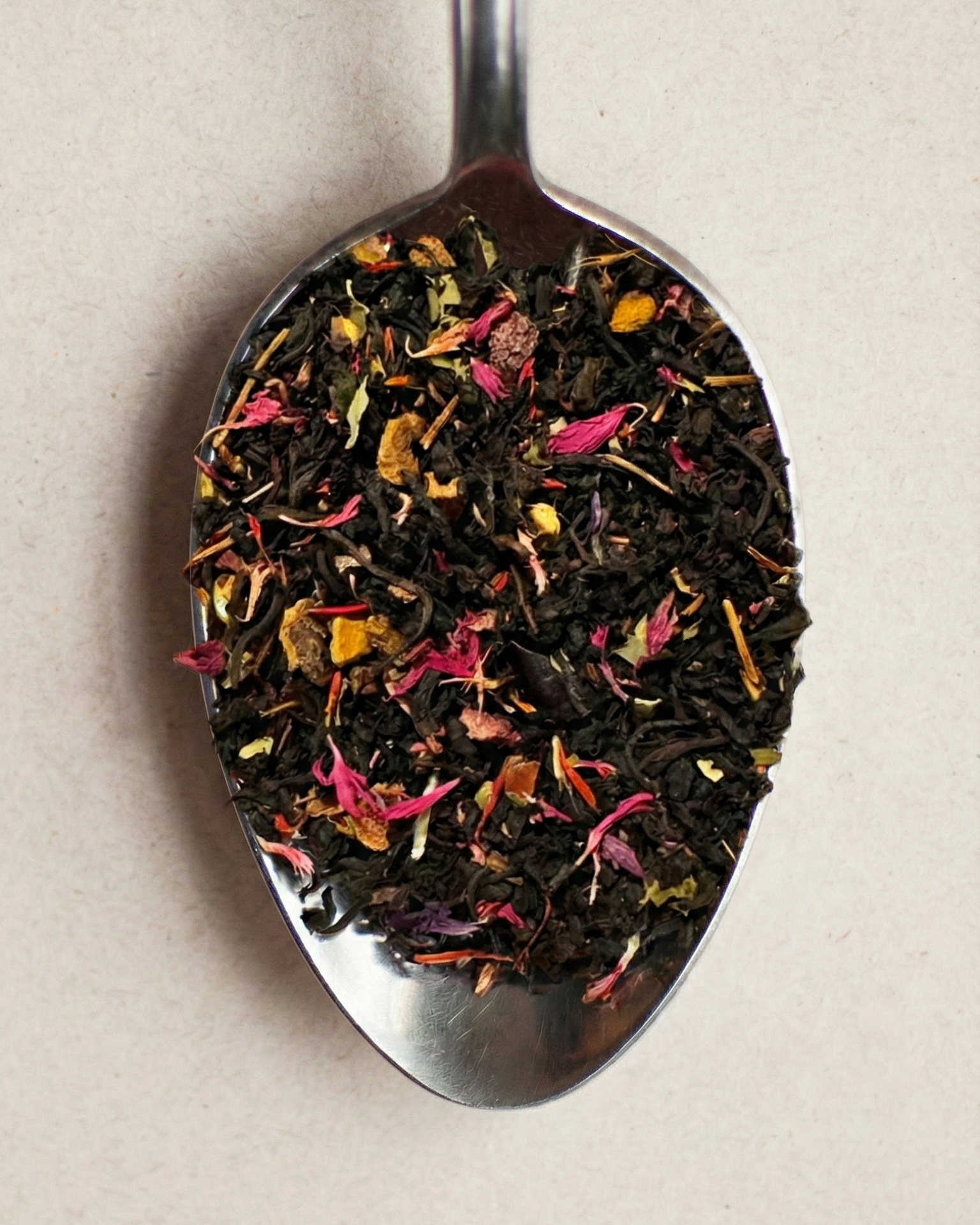 Metallic spoon filled with colorful dried tea leaves on a beige background