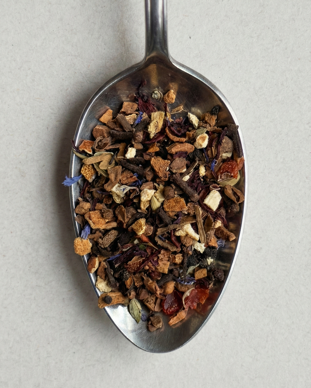 Spoon filled with a mix of dried herbs and spices on a light gray background