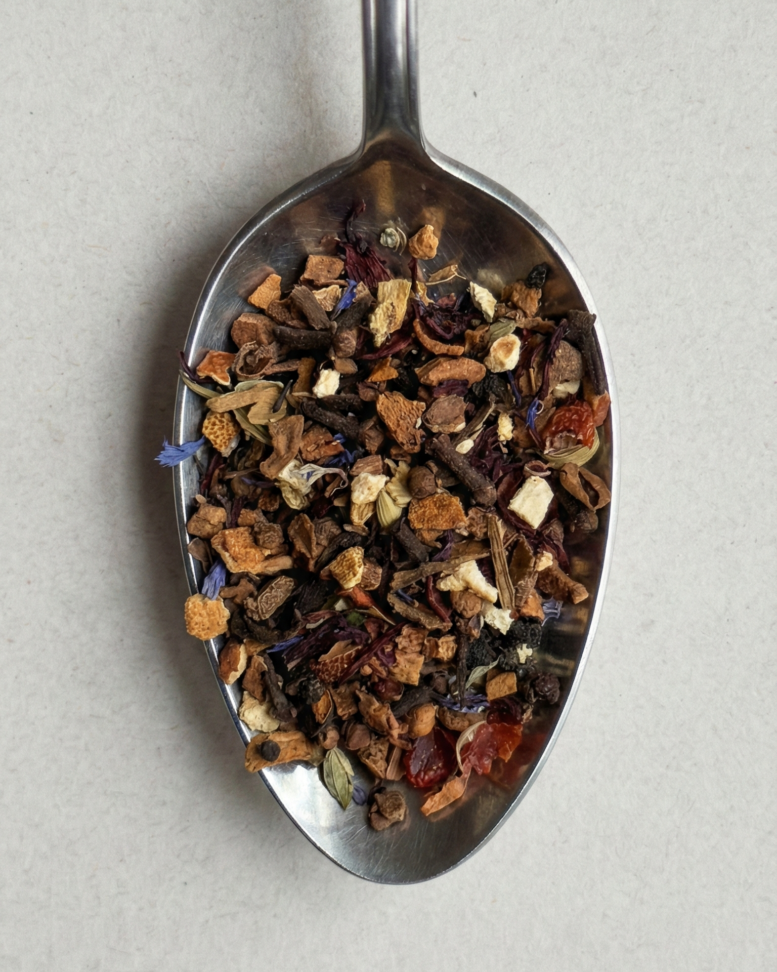 Spoon filled with a mix of dried herbs and spices on a light gray background
