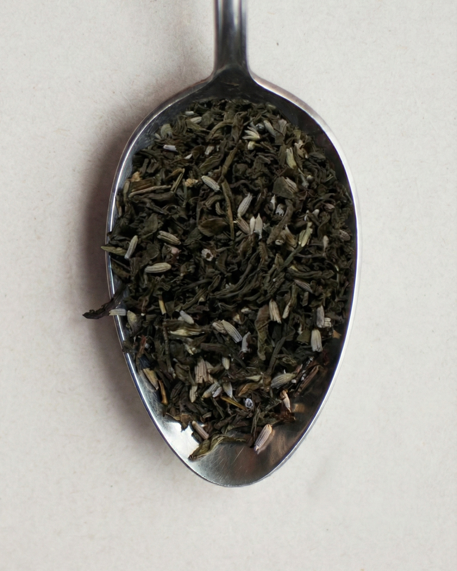 Tea leaves on a metal spoon against a light background