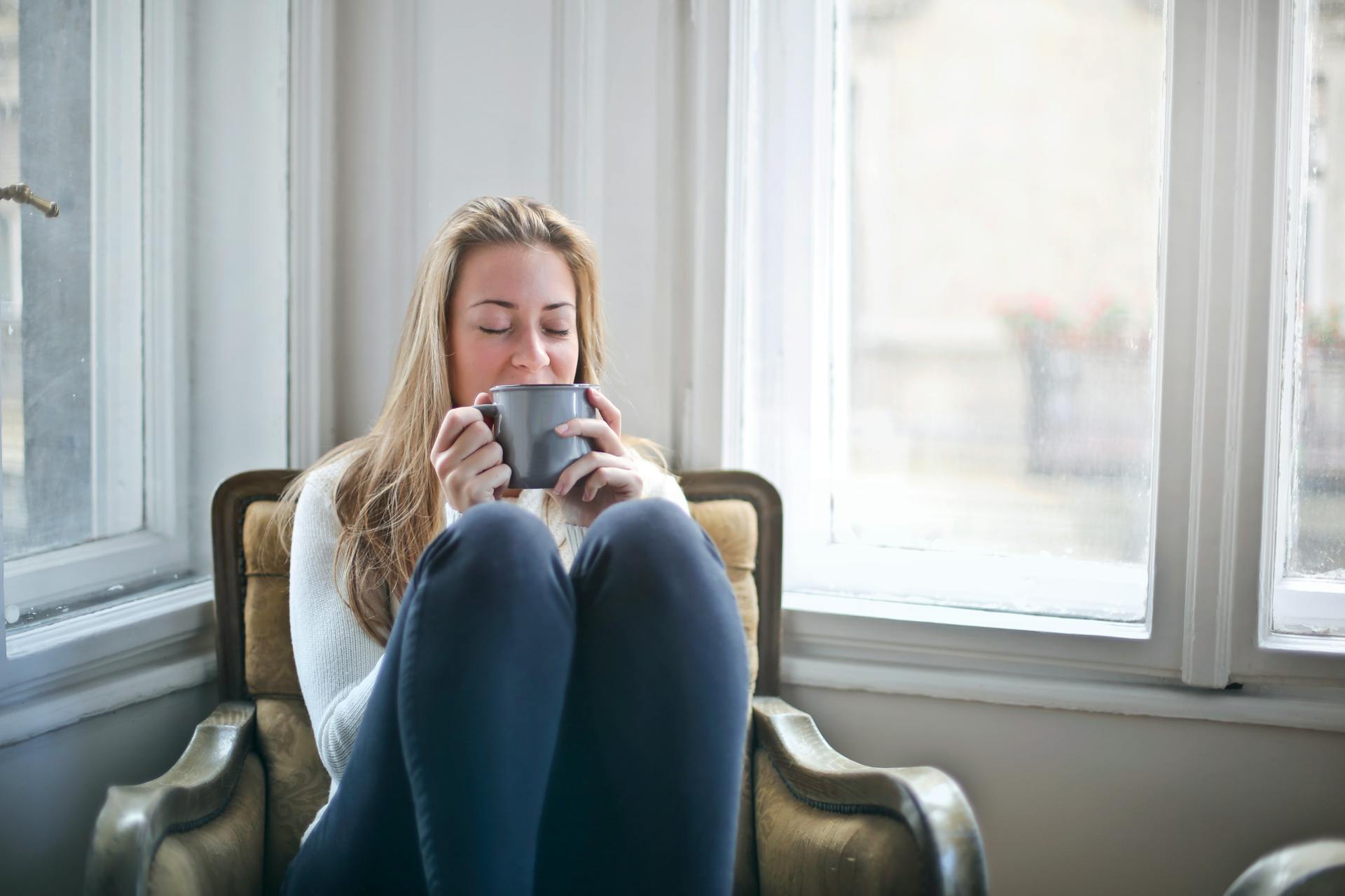 Woman sitting in a chair holding a mug in a room with large windows.
