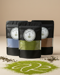 Three black tea bags with visible labels on a beige surface with scattered tea leaves.